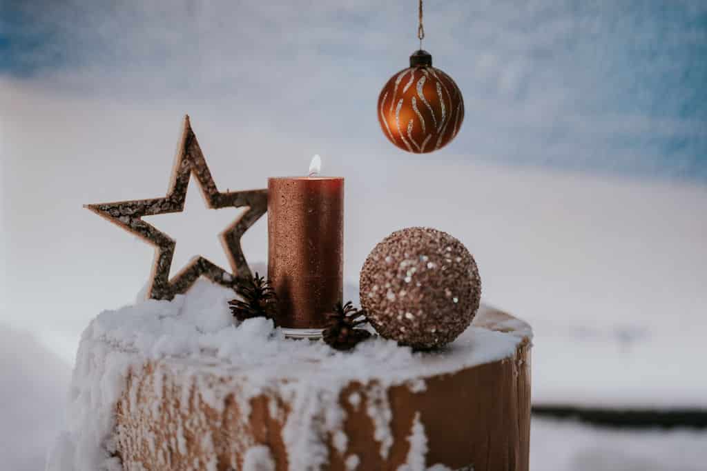 Kerze, Kugel und Stern auf Holzstamm im Schnee